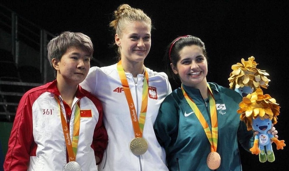 Na zdjęciu znajdują się trzy kobiety w sportowych bluzach i z medalami na szyjach. W środku stoi Natalia Partyka. 