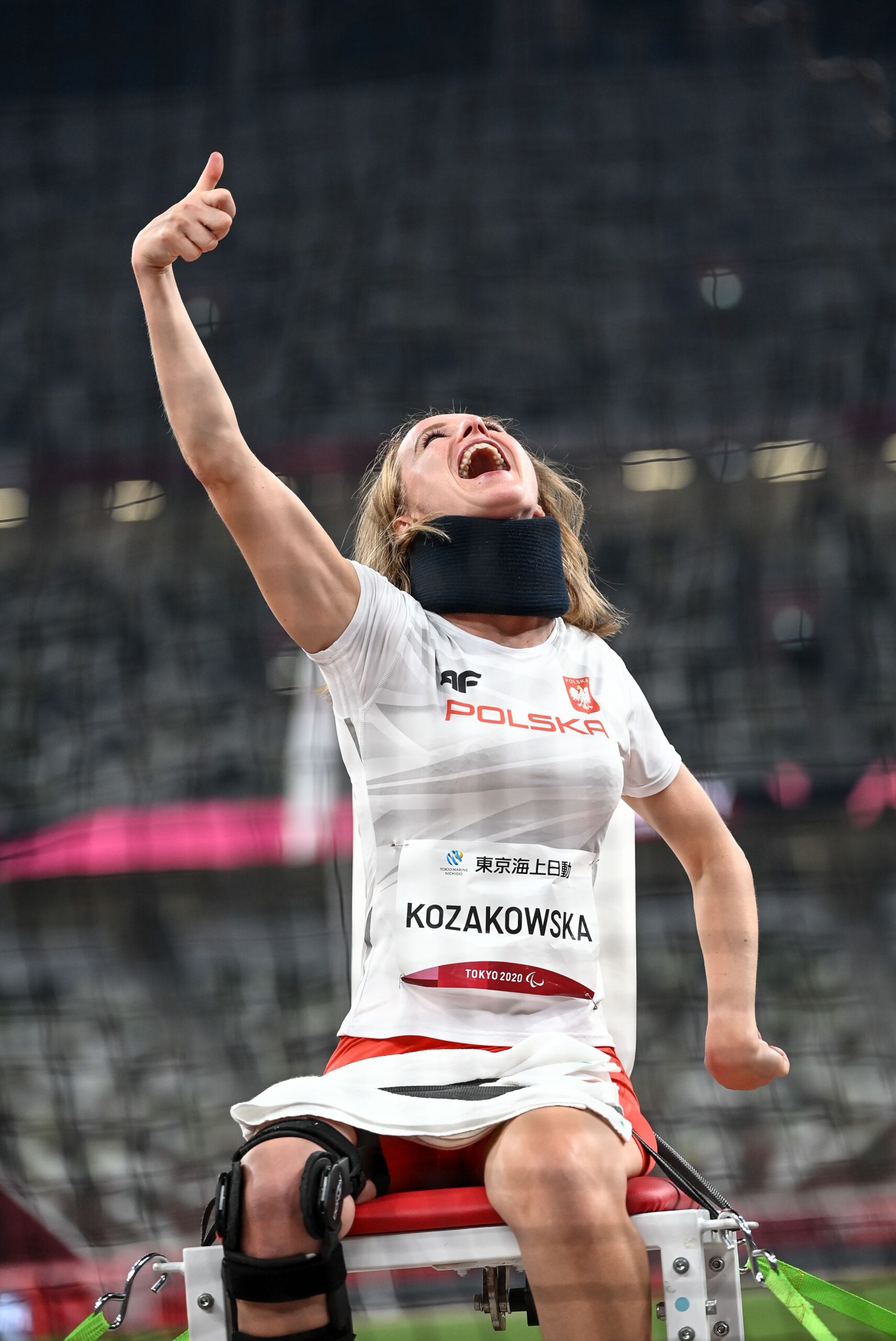 Na zdjęciu znajduje się uśmiechnięta Róża Kozakowska z uniesioną ręką, na stadionie sportowym.