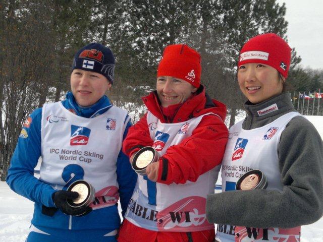 Na zdjęciu znajdują się trzy kobiety w narciarskich strojach, które trzymają medale. W środku stoi uśmiechnięta Katarzyna Rogowiec.