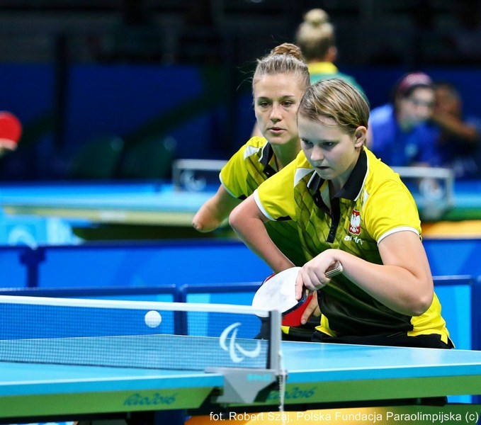Na zdjęciu znajdują się dwie dziewczyny, które w jednej drużynie grają w tenisa stołowego.