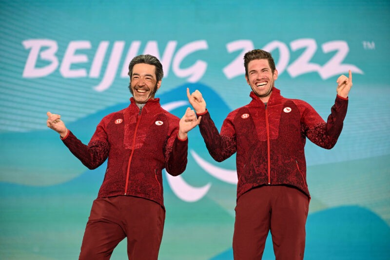 Na zdjęciu znajduje się dwóch uśmiechniętych mężczyzn w strojach sportowych.