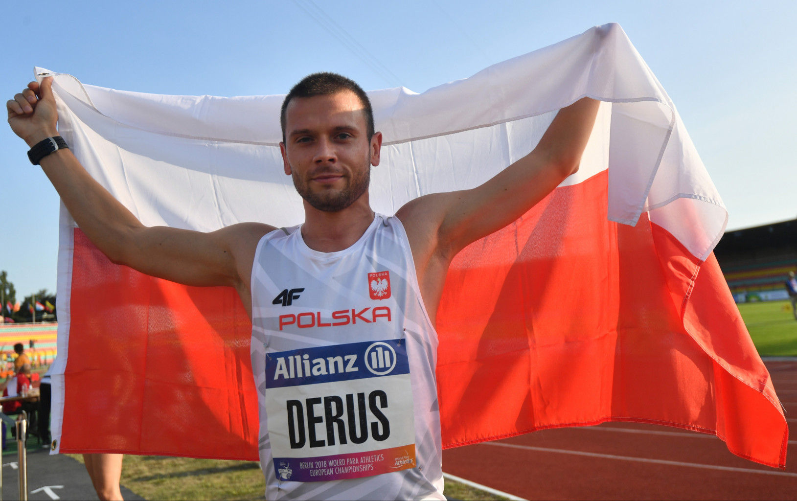 Na zdjęciu znajduje się mężczyzna (Michał Derus), który trzyma dużą flagę Polski za plecami.