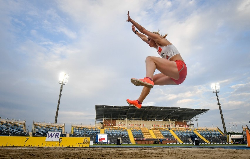 Zdjęcie przedstawia kobietę (Karolinę Kucharczyk), która na stadionie skacze w dal.
