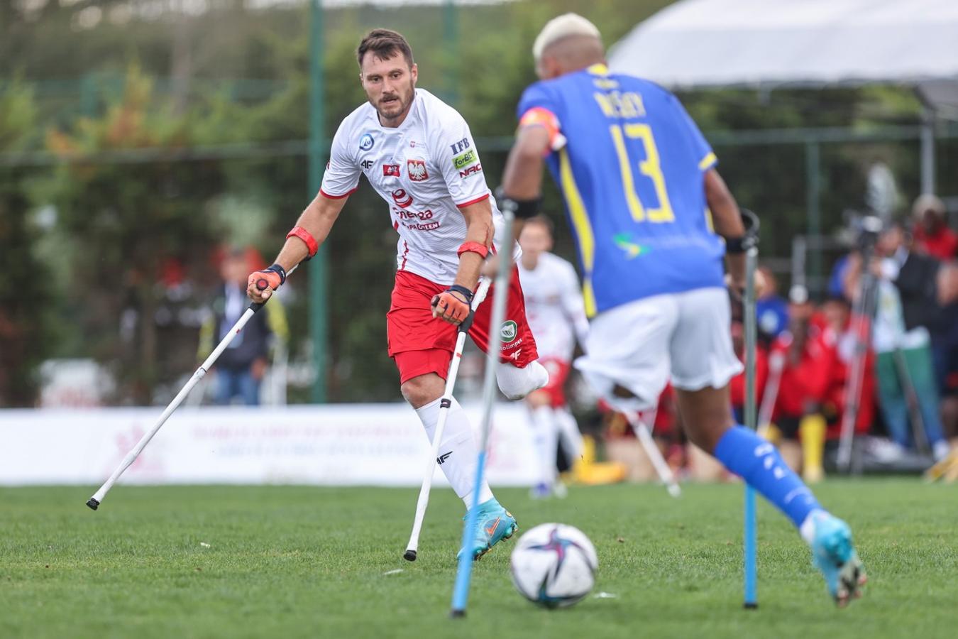 Mężczyzna w stroju reprezentacji Polski bez lewej nogi gra w piłkę nożną na boisku.