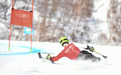 Mężczyzna w stroju reprezentacji Polski, jedzie na mono-ski (specjalnej narcie, na której człowiek porusza się w pozycji siedzącej)