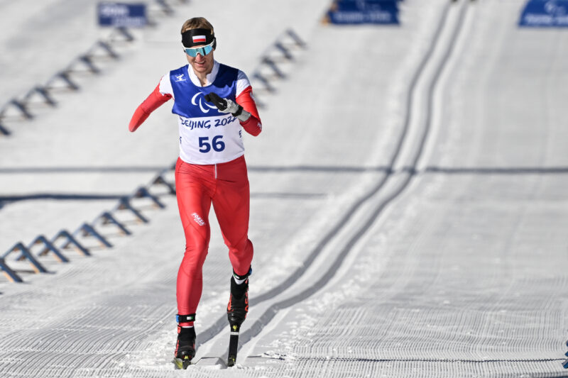 Mężczyzna w stroju reprezentacji Polski bez prawej ręki, biegnie na nartach.