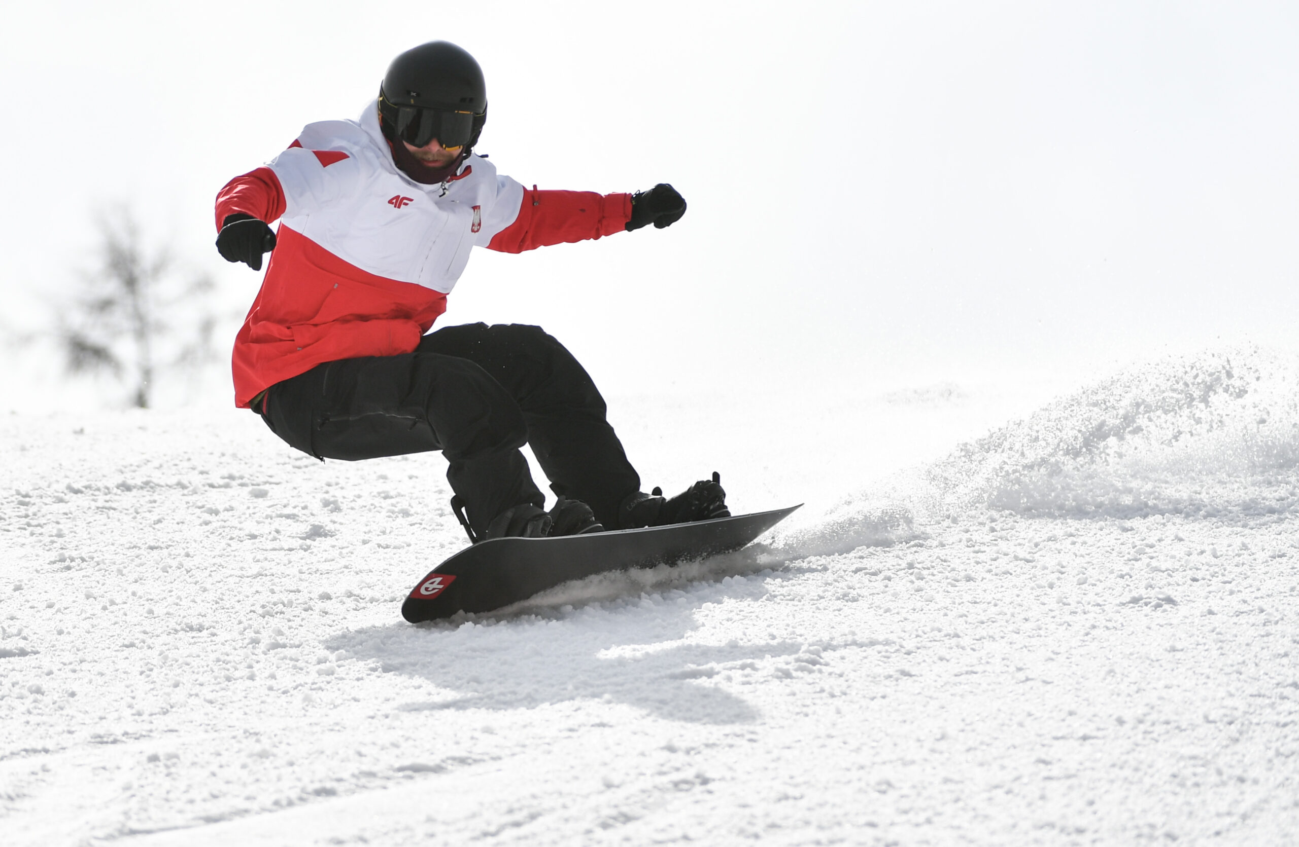 Mężczyzna w stroju reprezentacji Polski jedzie na desce snowboardowej.