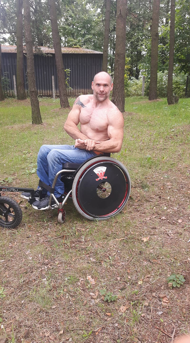 Muskularny mężczyzna z gołym torsem na wózku pręży mięśnie. 
