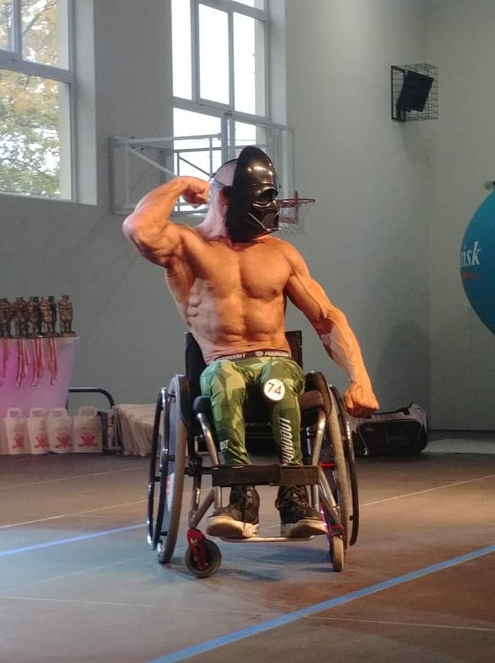 Muskularny mężczyzna na wózku pręży mięśnie. Na twarzy ma maskę Lorda Vadera.