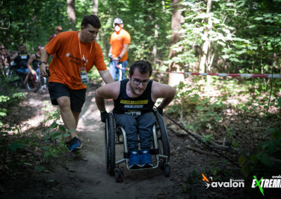 Uczestnik Wheelmageddonu jedzie na wózku przez las, a pracownik Fundacji mu pomaga.