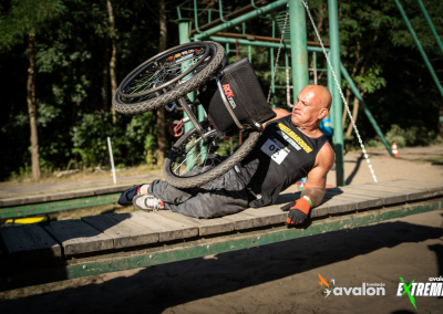 Łysy mężczyzna leży na drewnianej platformie i podnosi wózek aktywny.