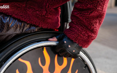 Zdjęcie osoby w puchowej czerwonej kurtce, w skórzanych rękawiczkach bez palców, trzyma uchwyt wózka aktywnego.