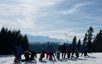Grupowe zdjęcie ludzi na szczycie ośnieżonej góry, Częśc osób znajduje się na nartach, a część na monoski w pozycji siedzącej.